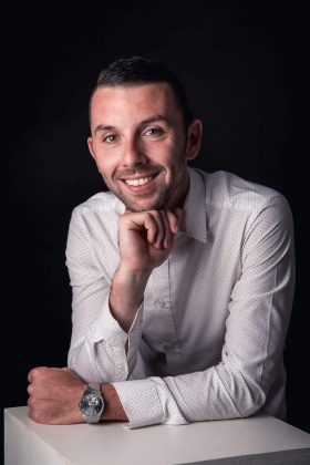 Photo de profil business d'un homme en chemise blanche à pois, affichant un sourire confiant et professionnel face à l'objectif