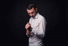 Homme en chemise blanche ajustant son bouton de manchette, regardant vers le bas, posant élégamment pour un shooting photo professionnel