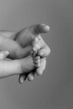 Photo de détail montrant les petits pieds d'un bébé tenus dans les mains des parents, photographie de naissance artistique en noir et blanc