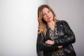 Femme active posant les bras croisés appuyée contre un mur blanc, attitude assurée et professionnelle pour un shooting corporate