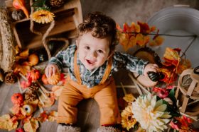 Bébé souriant assis dans un décor automnal avec des citrouilles et des feuilles mortes, séance photo à thème à Wattignies