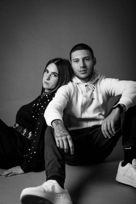 Jeune couple assis au sol en studio, adoptant une pose décontractée et moderne, photographie en noir et blanc