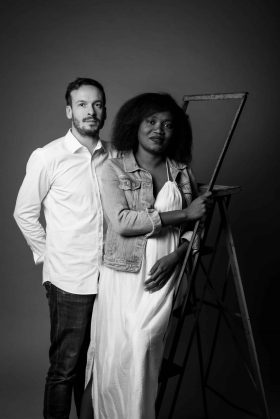Photo de grossesse en noir et blanc d'une future maman et d'un futur papa posant debout à côté d'une échelle vintage dans notre studio à Lille