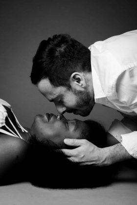 Photo noir et blanc d'un futur papa penché au-dessus de la future maman allongée, moment intime et tendre capturé lors d'un shooting grossesse à Lille