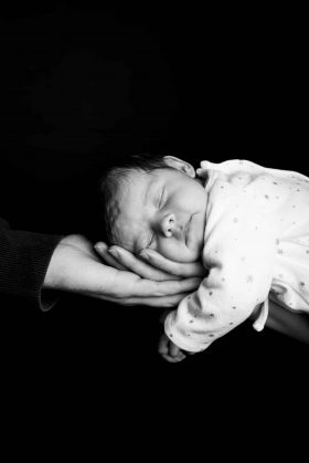Portrait noir et blanc d'un nouveau-né dormant paisiblement sur l'avant-bras de son papa lors d'une séance naissance à Lille