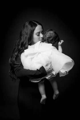 Maman câlinant sa fille portant une robe blanche de dos, portrait élégant en noir et blanc réalisé dans notre studio photo à Linselles